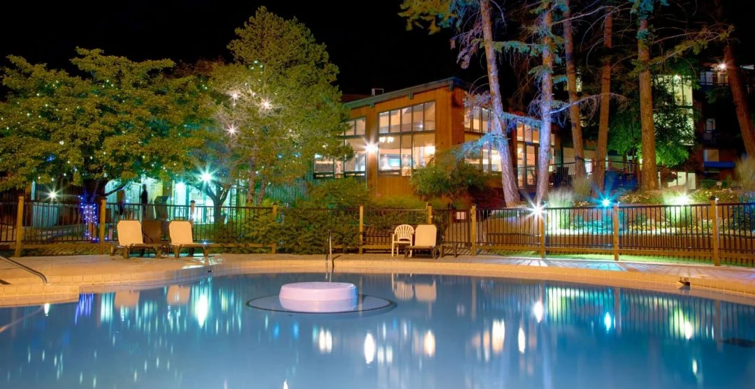 outdoor hot springs pool at night reflecting lights, building and trees in backgound
